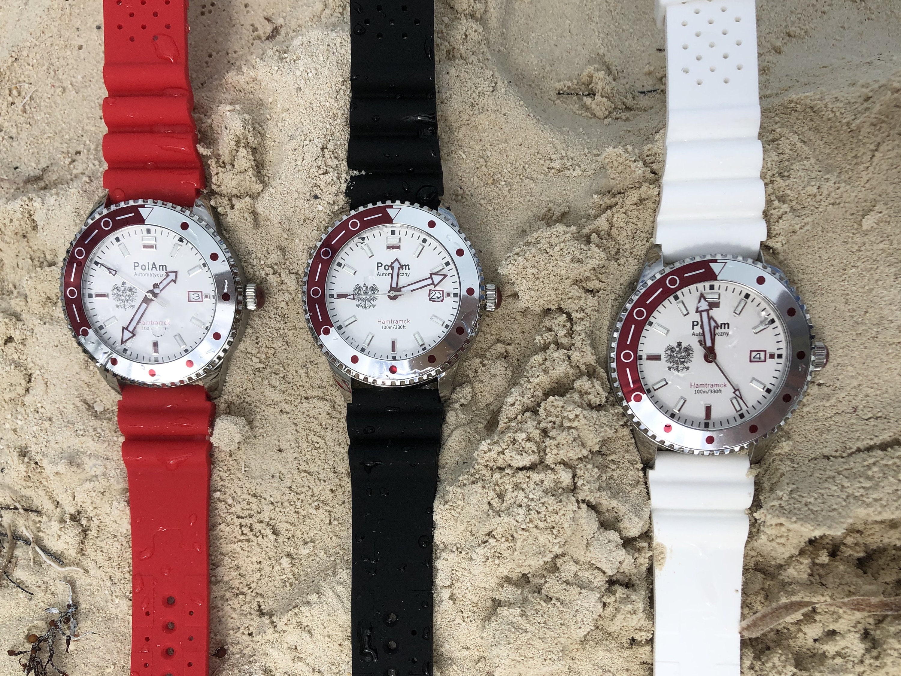 Three PolAm Hamtramck watches in red, black, and white rubber straps on sand